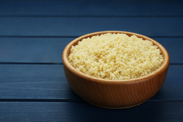 Bowl of tasty couscous on blue wooden table, closeup. Space for text