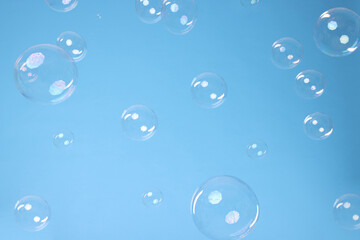 Many beautiful soap bubbles on light blue background