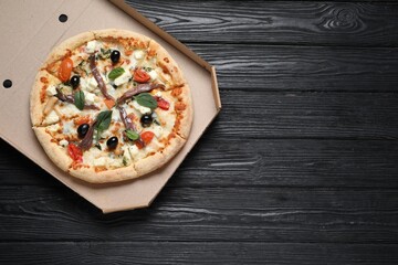 Tasty pizza with anchovies, basil and olives on black wooden table, top view. Space for text