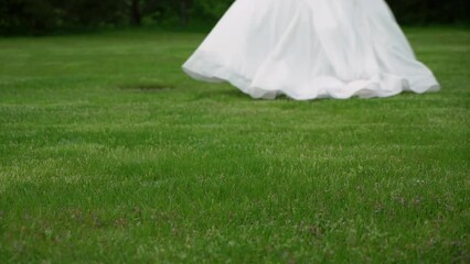 A bride in a long white wedding dress and high-heeled shoes walks on lawn. Wedding ceremony, reception. Woman run away slowmotion.