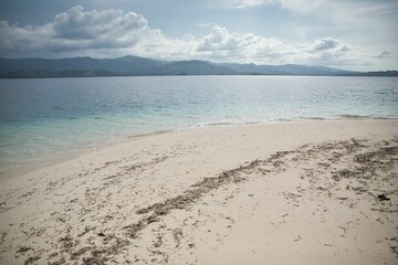 Paradisiacal shot of a white beach in Riung on Flores, with a range of hills in the background.