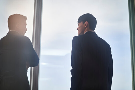 two asian businesspeople talking chatting standing by the window talking chatting in office
