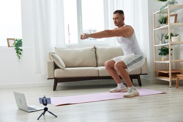 Fototapeta na wymiar Man sports, watching a workout tape on his phone and repeating exercises sports blogger with dumbbells, pumped up man fitness trainer works out at home, the concept of health and body beauty