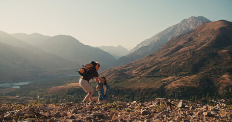 Caucasian couple hiking together with backpacks, helping each other on their way up the mountains....