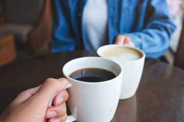 Closeup image of a couple people clinking white coffee mugs in cafe