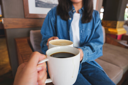 Closeup image of a woman and a man clinking white coffee mugs in cafe