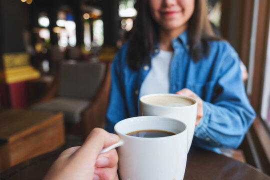 Closeup image of a woman and a man clinking white coffee mugs in cafe