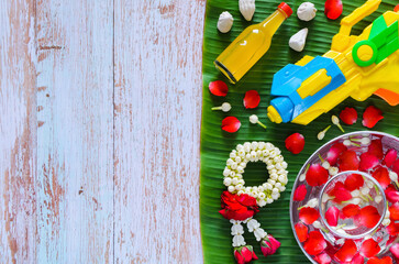 Thailand songkran festival background with water gun, garland and scented water put on banana leaf with wooden background.