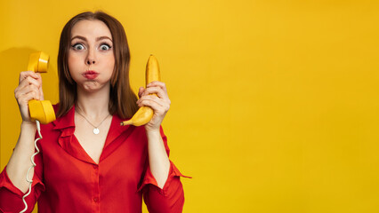 Funny face with a banana and a phone handset. A young woman with a smile holds a banana in her hand. Funny expressions. The concept of nutrition. Yellow style. Vitamins. Empty space for your text or