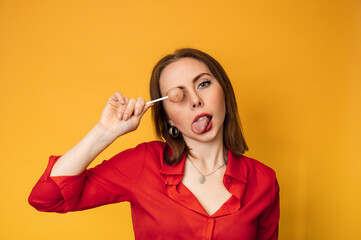 A surprised young funny girl is holding a lollipop in her hands and fooling around.