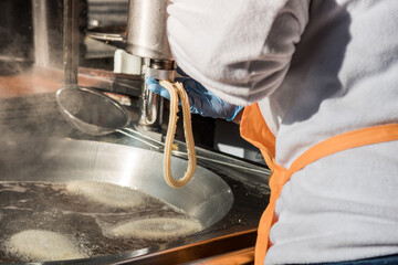 Detail of worker making churros at the machine on the industrial metal kitchen.