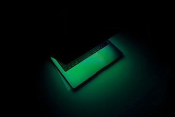 Laptop with backlit keyboard at night. Copy space. Illuminating green neon light. Abstract horizontal poster about privacy information, security and technology