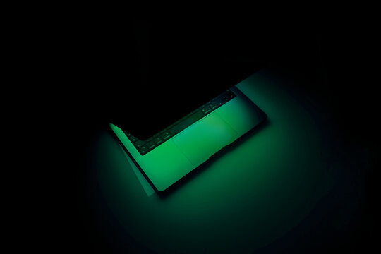 Laptop with backlit keyboard at night. Copy space. Illuminating green neon light. Abstract horizontal poster about privacy information, security and technology