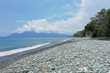 Fototapeta na wymiar Close-up of blue stones on the beach of Pantai Batu Biru, the Blue Stone Beach, in the background a hill, in Ende on Flores.
