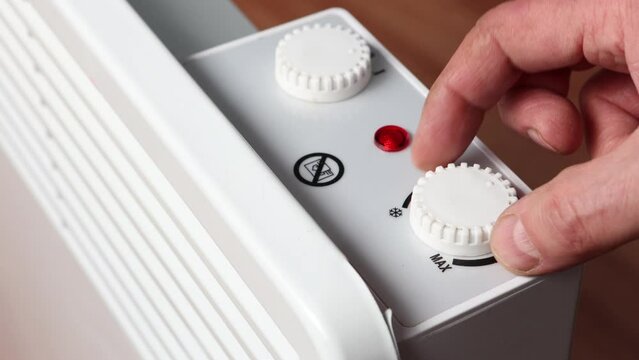 Adjusting temperature on thermostat dial of convector heater.
