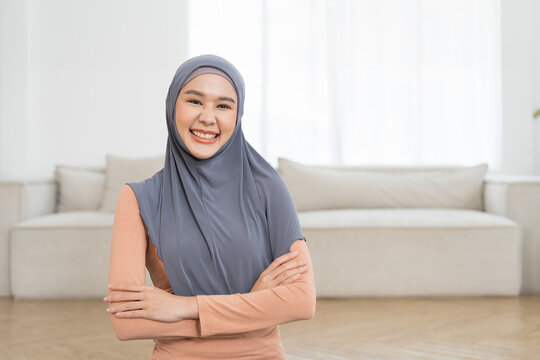 Beautiful smiling Asian young muslim woman wear hijab standing with crossed arms and looking to camera at home