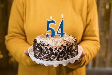 Woman holding a festive cake with number 54 candles while celebrating birthday party. Birthday...