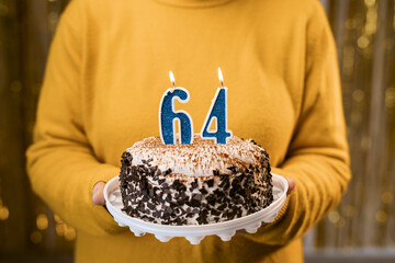 Woman holding a festive cake with number 64 candles while celebrating birthday party. Birthday...
