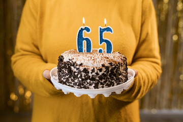 Woman holding a festive cake with number 65 candles while celebrating birthday party. Birthday holiday party people concept.