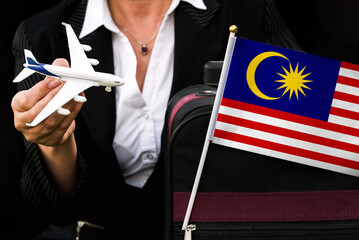 business woman holds toy plane travel bag and flag of Malaysia
