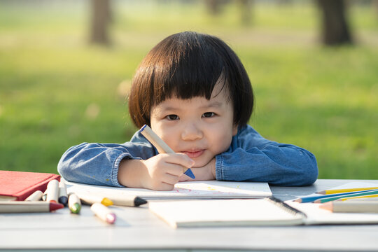 asian little girl drawing on paper in garden.