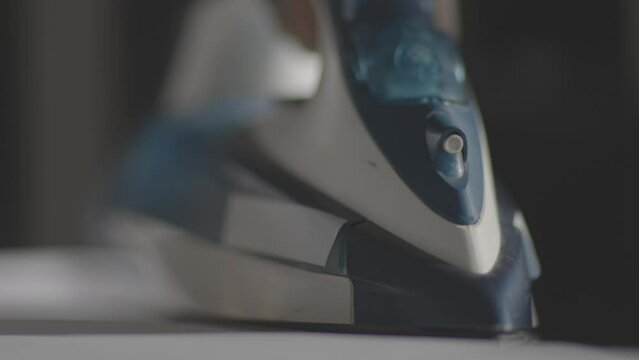 Selective focus of female hand irons white clothes with steam iron on an Ironing board. Push button of steam humidifier, laundry moistening function. Ironing linen using hot steam