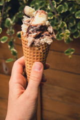 Female hand holding delicious american vanilla chocolate ice cream. Tasty homemade icecream Gelato in the waffle cone. Gluten free vegan dairy free ice cream. 