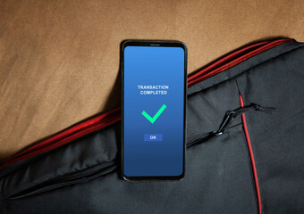 money received notification in a mobile phone screen, phone alongside with bag on table