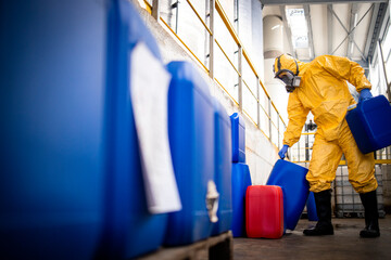 Worker wearing protection suit and gas mask working in chemicals production factory. Carrying acid plastic containers for zinc galvanizing industry.