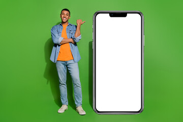 Full size photo of young guy point finger huge smartphone recommend online shop isolated on green color background