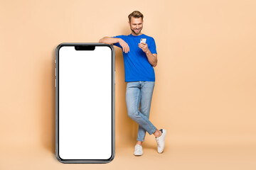 Full body portrait of positive blogger man use telephone empty space display isolated on beige color background