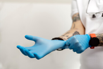 Obraz premium On a white background, a man with tattooed hands puts on disposable gloves. The concept of protection and safe work with the patient.