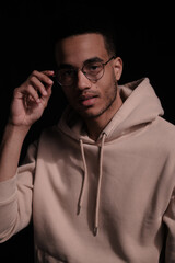 Obraz premium Portrait of a cheerful young african american man 20s wearing casual hoody and glasses against black background. copy space isolated