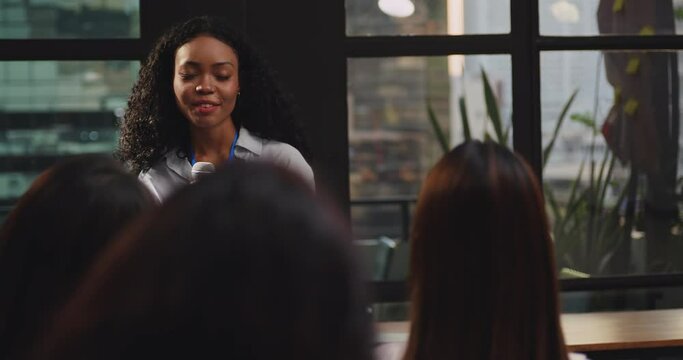 Confident young businesswoman or speaker sharing ideas with colleagues or audience during company seminar.