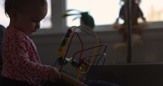 1 year old girl plays with her toy set in living room - side profile