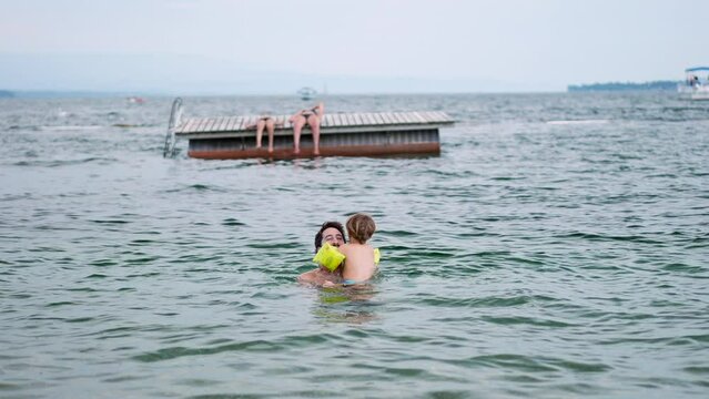Father bonding with baby son at lake water. Child wearing inflatable rollup arm bands. Fatherhood lifestyle concept swimming together