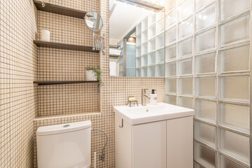 Stylish and simple bathroom design with beige mosaic and toilet and glass block wall with shelves....