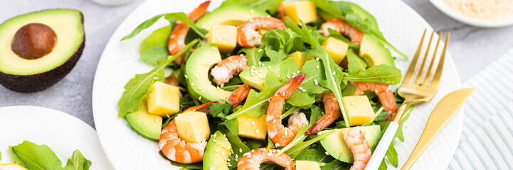 Flat lay of Healthy salad plate. Fresh seafood recipe. Grilled shrimps and fresh vegetables (avocado, arugula, mango) on gray concrete background. 