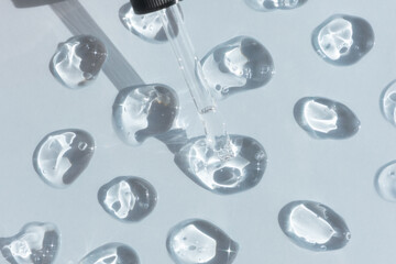 Drops of serum or hyaluronic acid gel with a pipette on a gray background. Smears of cosmetic skin care products. Wellness and beauty concept.