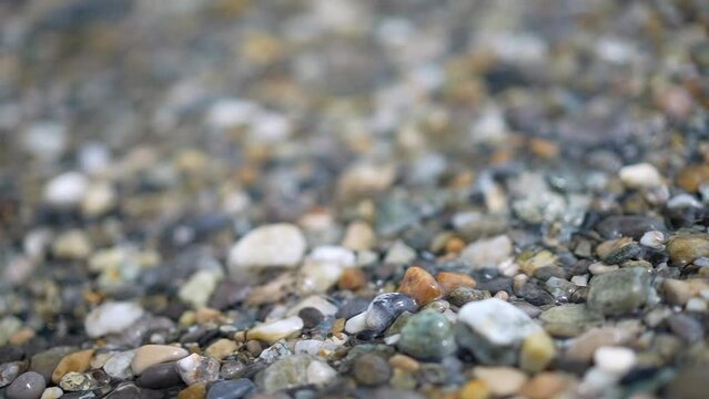Many diverse rocks at shore with water in slow motion 240 fps closeup of beach lake gravel