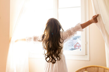 Young woman open a curtains and stretching in bed after waking up, sunlight in morning and open the curtain with lens flare at her home