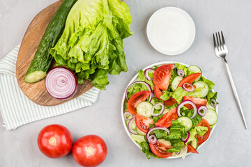 Healthy vegetarian dish on table, vegetable salad with fresh tomato, cucumber, lettuce, red onion on gray concrete background. Diet menu. Top view. Flat lay, mockup, template with copy space