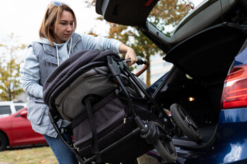 Obraz na płótnie Canvas mom driver puts baby stroller in car trunk