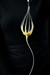 Preparation of sweet cream. Kitchen whisk with white sweet cream. On a black background. Kitchen...