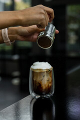 A glass of iced coffee is positioned on the countertop of a bar.