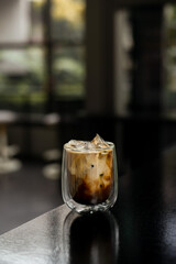 A glass of iced coffee is positioned on the countertop of a bar.