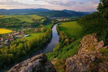 Spring landscape with blooming fields, green meadows and a meandering river in a valley under rocks.