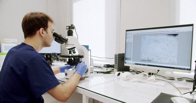 Scientist in sperm laboratory. Lab worker is regulating a microscope during research. Analyze sperm cells fertilizing ovum egg under microscope, doctor looking at human fertilization process.