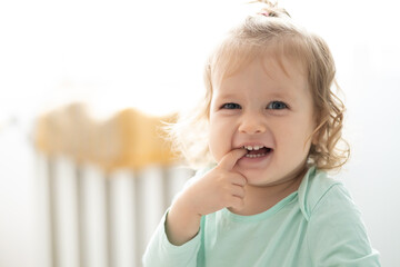 toddler girl smile and puts finger in mouth, authentic joy, bright concept - obrazy, fototapety, plakaty