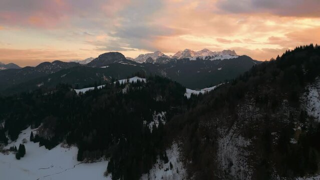 Mountain sunset in snowy landscape with snow, sunlight, forest and trees. Aerial drone view flying in cinematic alpine winter scenery in Austria Bavaria alps mountains valley. 4K UHD epic documentary.